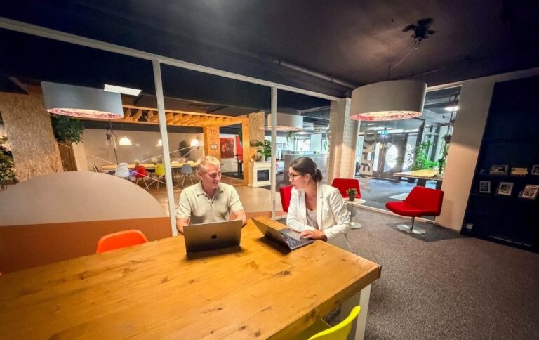 Ondernemer krijgt uitleg over de AI-verordening voor zijn website tijdens een overleg met laptops in het kenniscentrum van Kwaaijongens